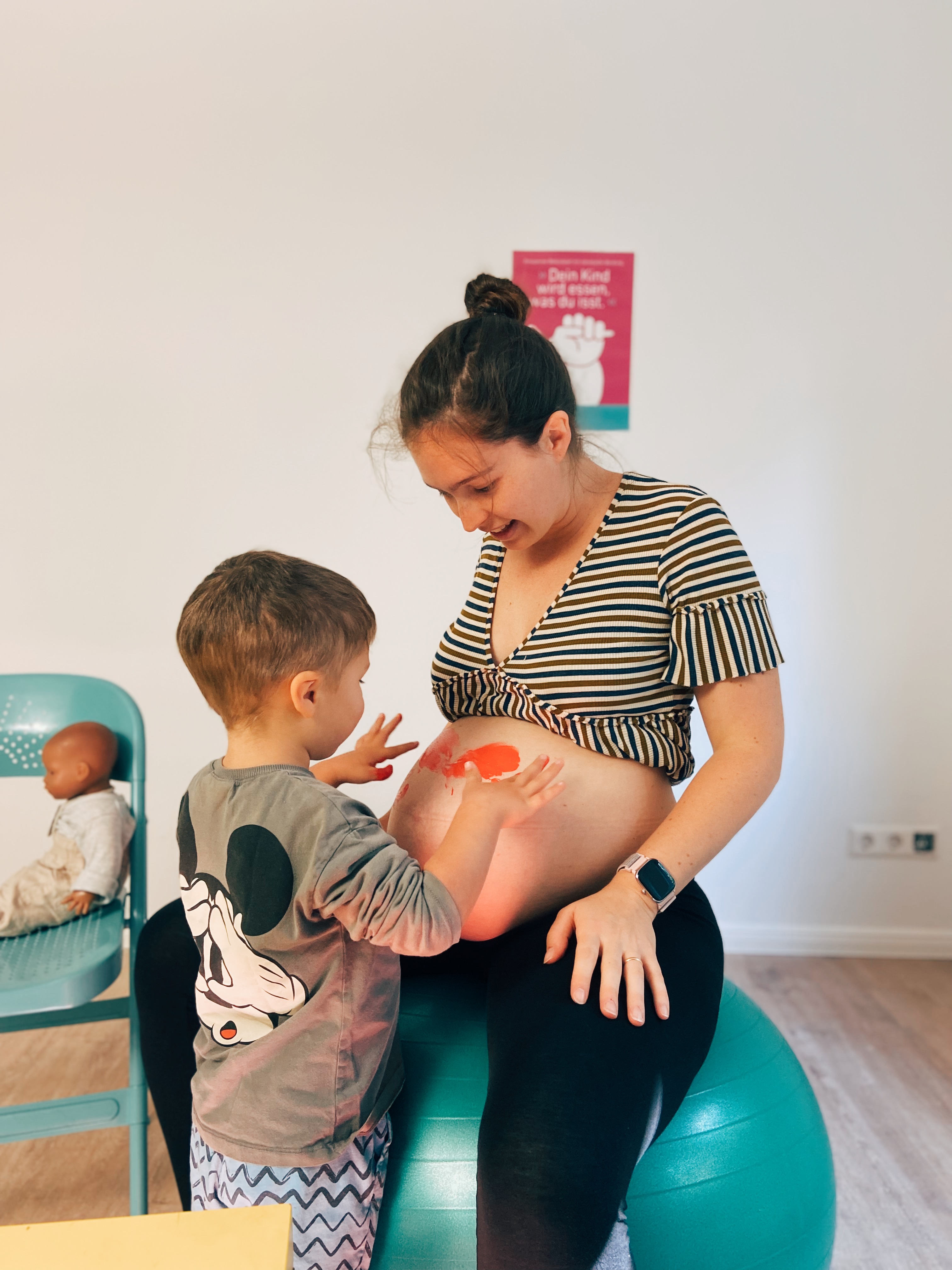 Ein Kind mahlt den Bauch einer Schwangere an.